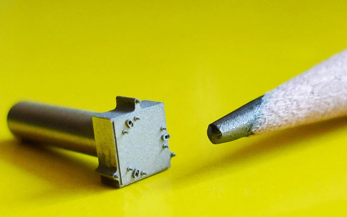 Tiny machined part on a shank beside a pencil tip